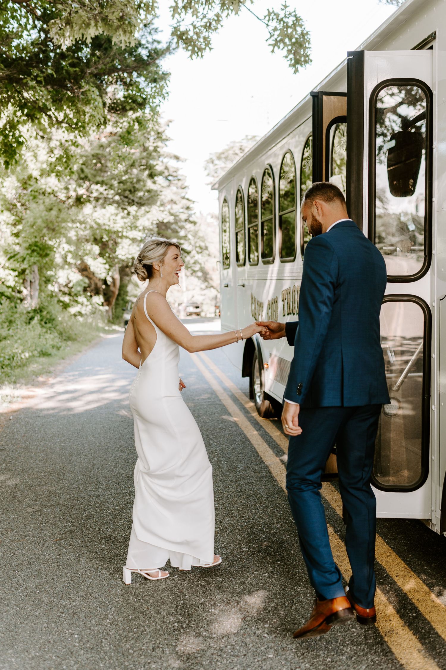 A couple in wedding attire playfully interacting near a vintage bus on their special day.