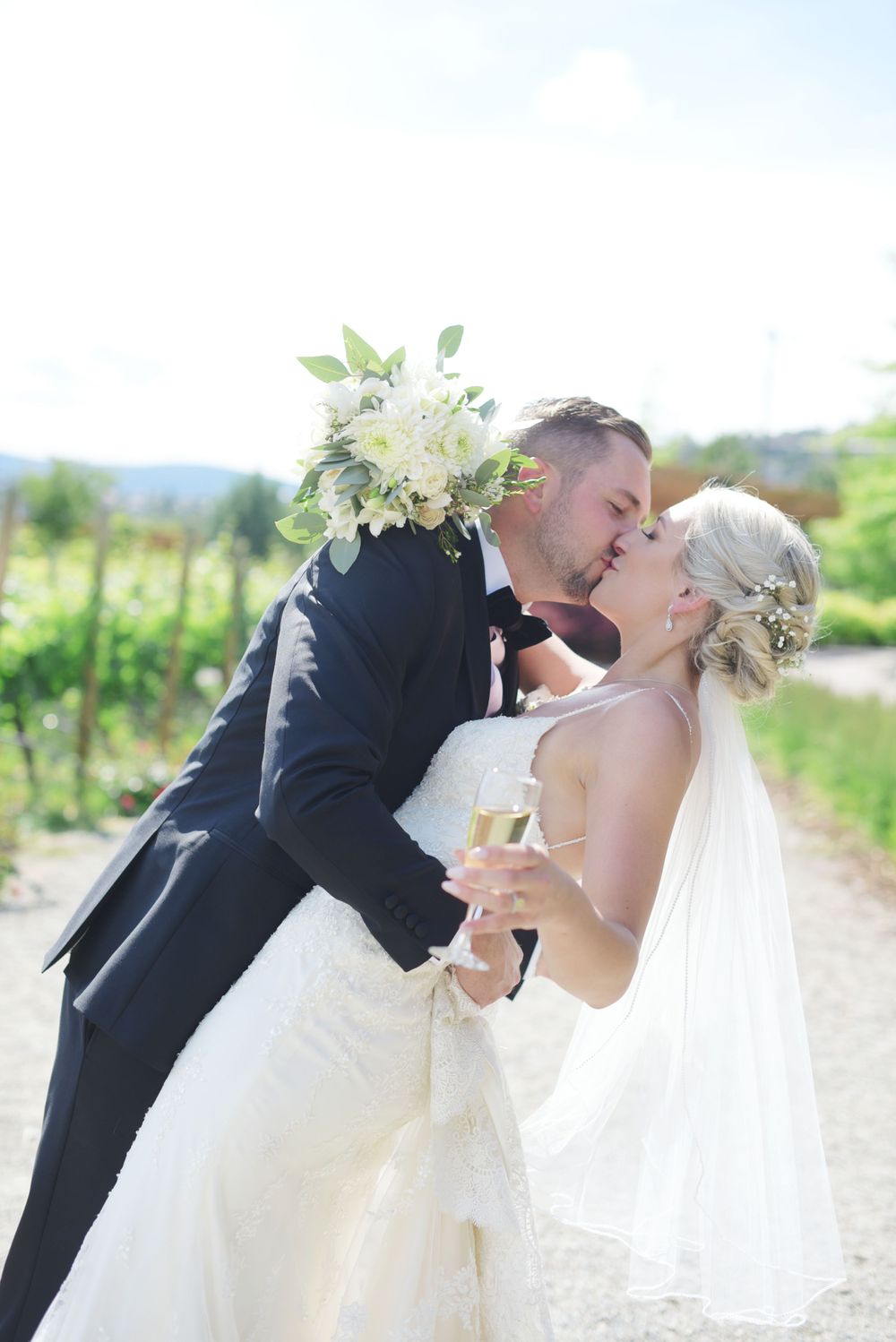 Romantic wedding kiss captured in vineyard setting with white floral bouquet at Quail's Gate Winery, Kelowna, B.C.