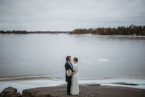 Hääpari seisoo rannalla meren äärellä, laaja maisemakuva vihkipäivästä – hääkuvaus Helsinki