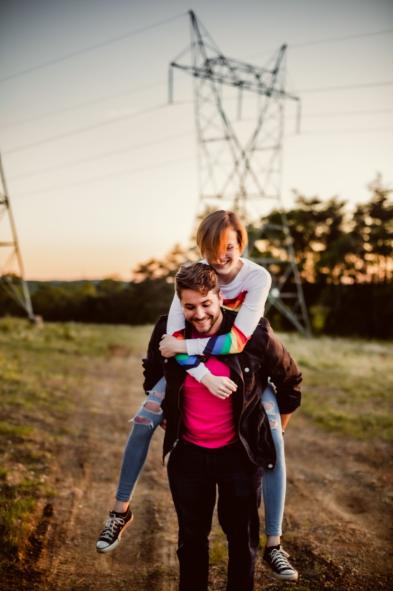 two people run through a field at sunset, with the one being carried on the other's back; they are laughing as they run