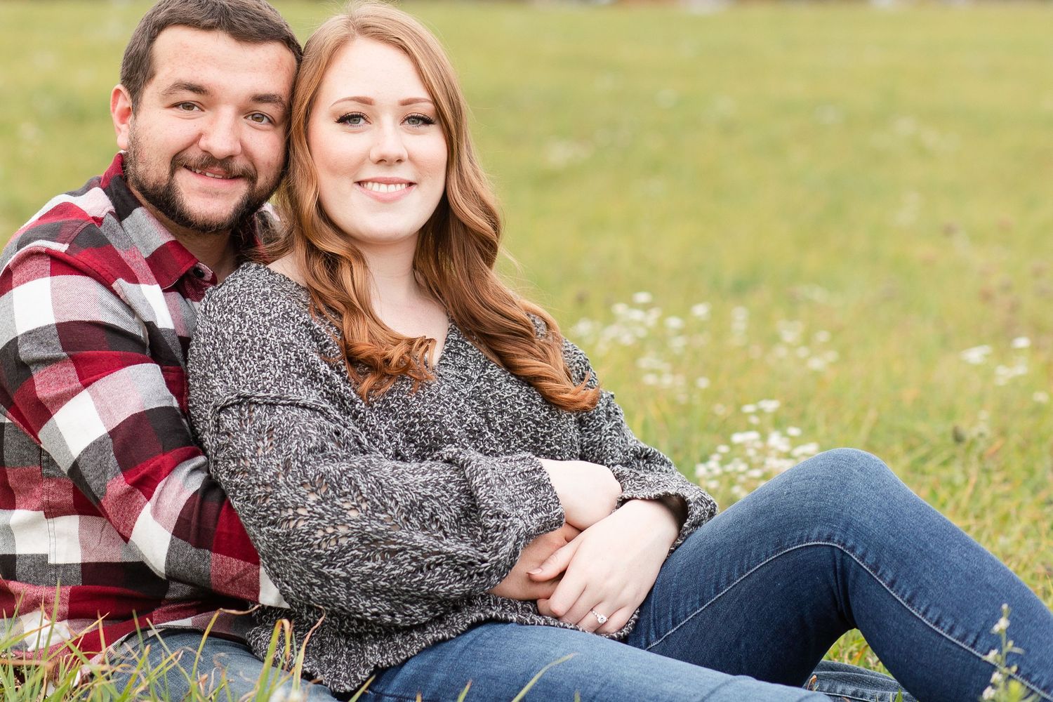 Couple relaxing in casual attire on grassy field during autumn.