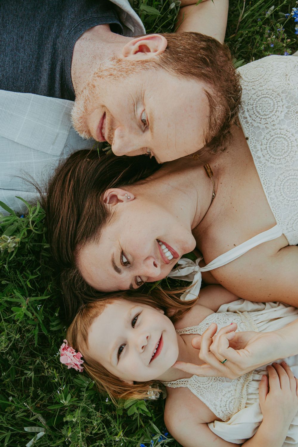 Family lying in grass together sharing intimate moment outdoors.