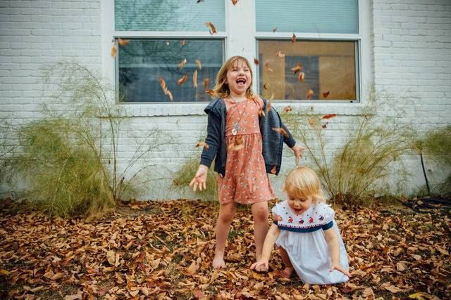 Children playing in fallen autumn leaves outside brick building.