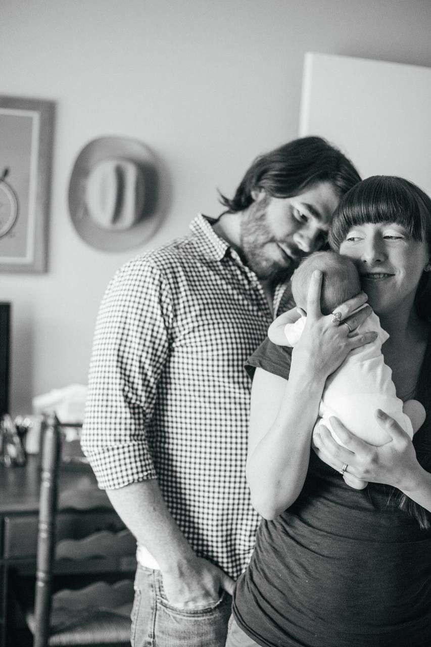 Family sharing an intimate black and white moment with their newborn baby at home.