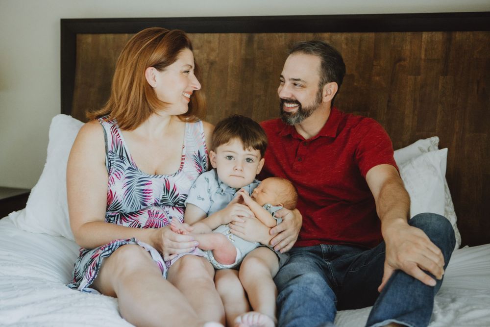 Family sitting together on a bed while holding and bonding with their young child in casual attire.