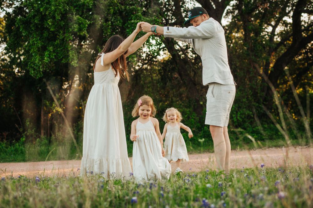 Family dancing together in a wildflower field at sunset wearing white dresses.