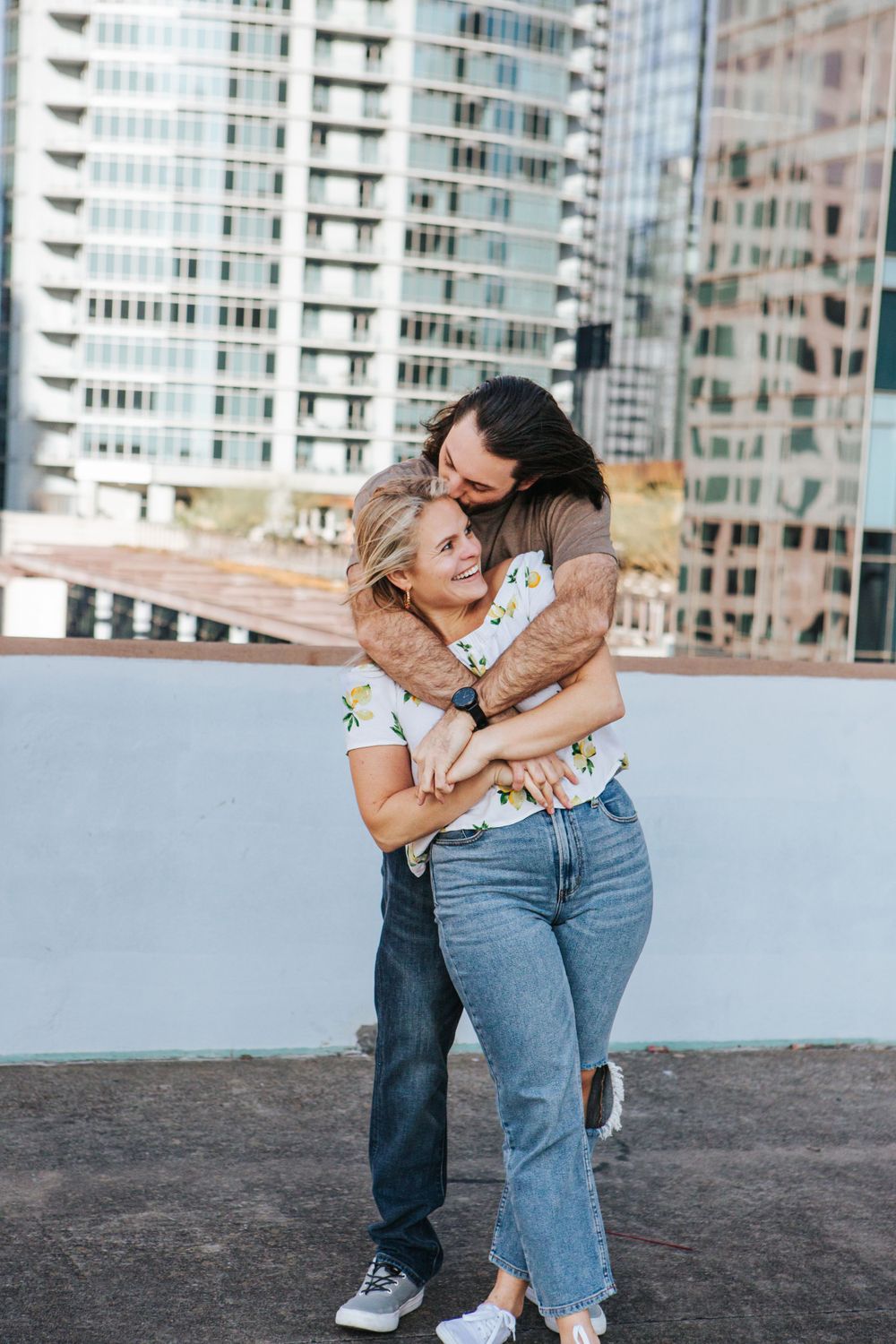 Couple embracing on urban rooftop with city buildings in background.