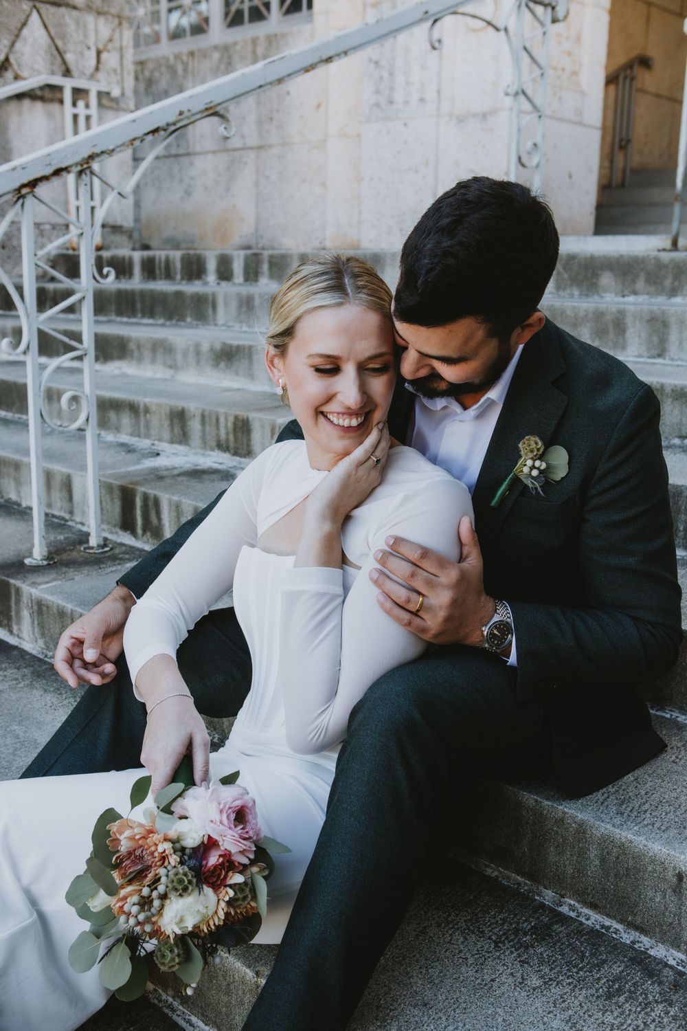Newlyweds sharing romantic moment on stone steps with bridal bouquet.