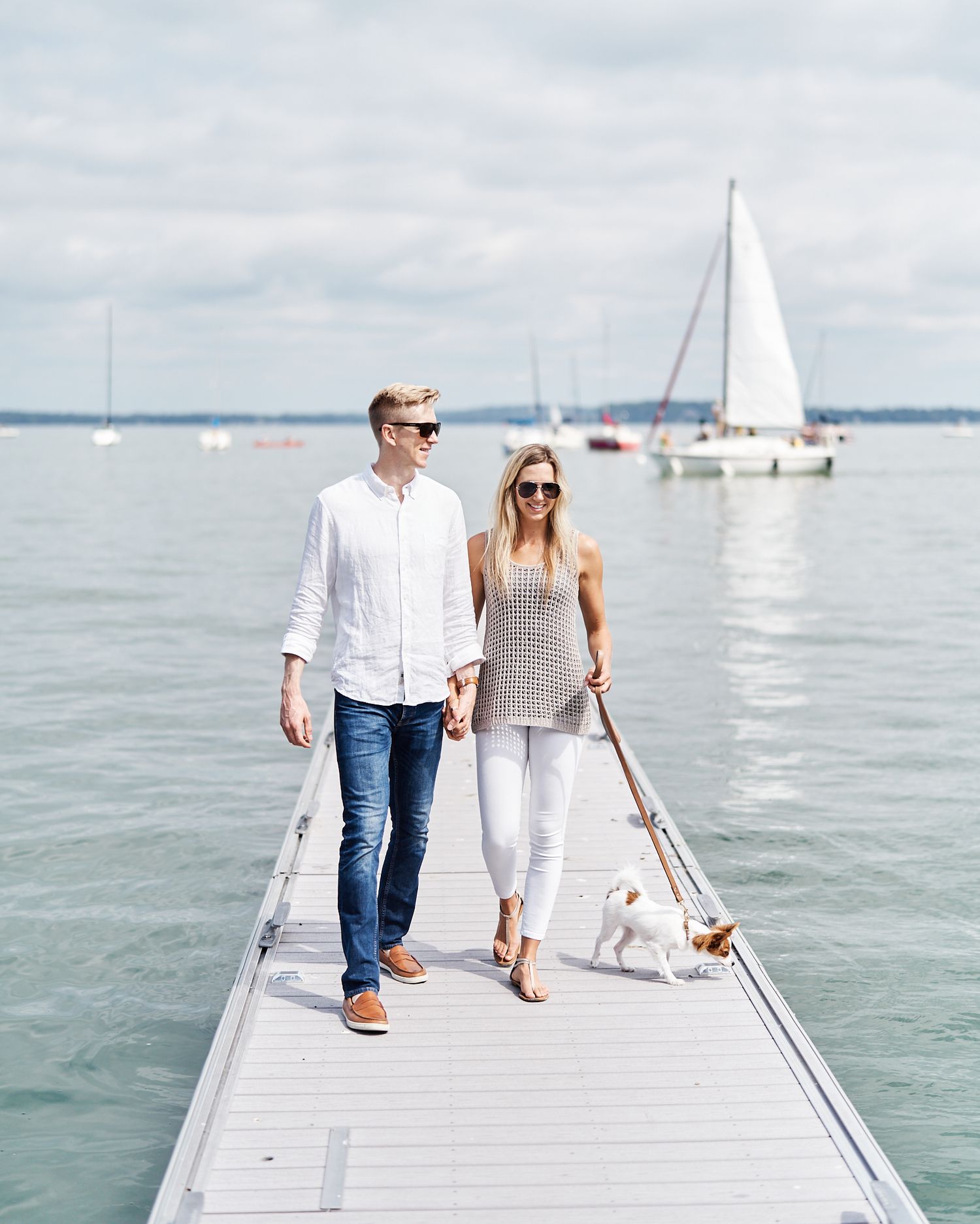 A couple walking their dog on a sunny day on a dock in Madison, Wisconsin photographed by Manzeck Photography for a lifestyle photo session.