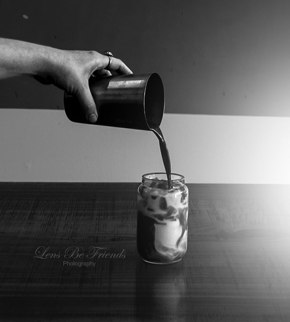 Black and white sequence showing liquid being poured into a small glass in dramatic lighting.