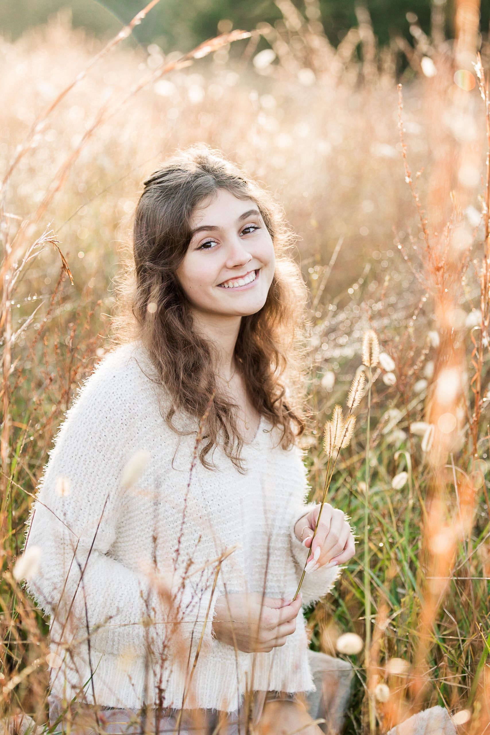 Senior girl sitting in field of tall grass in fall