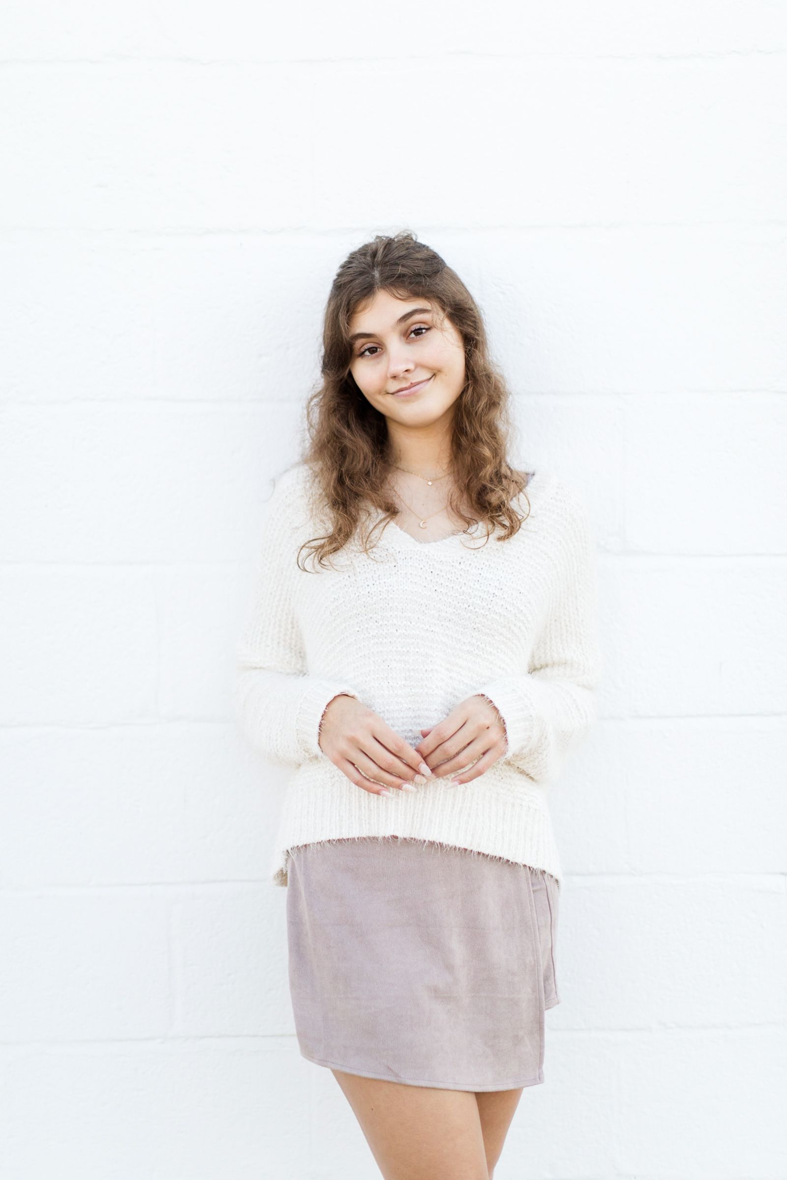 Senior girl leaning against white brick wall