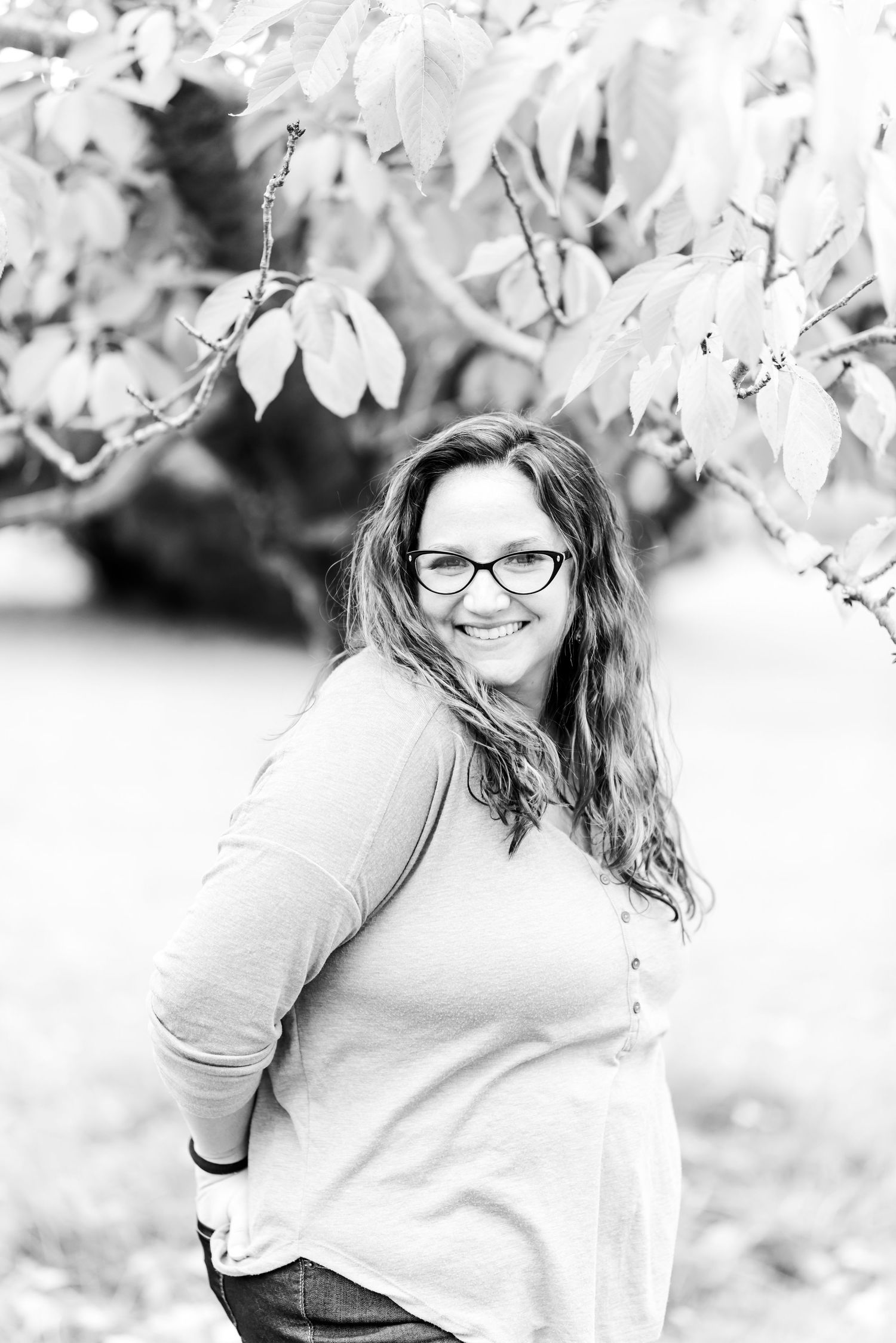 Black and white portrait of a woman smiling outdoors among spring tree branches.