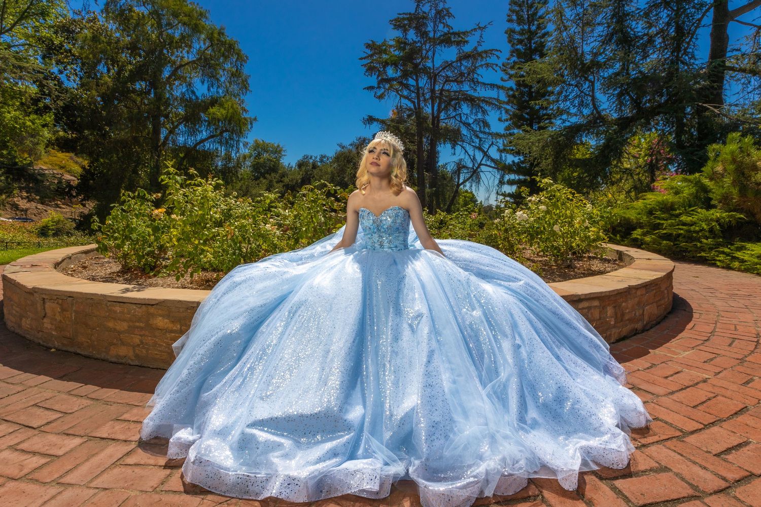 A stunning powder blue ball gown with sparkling details flows across brick pavers in a garden setting.
