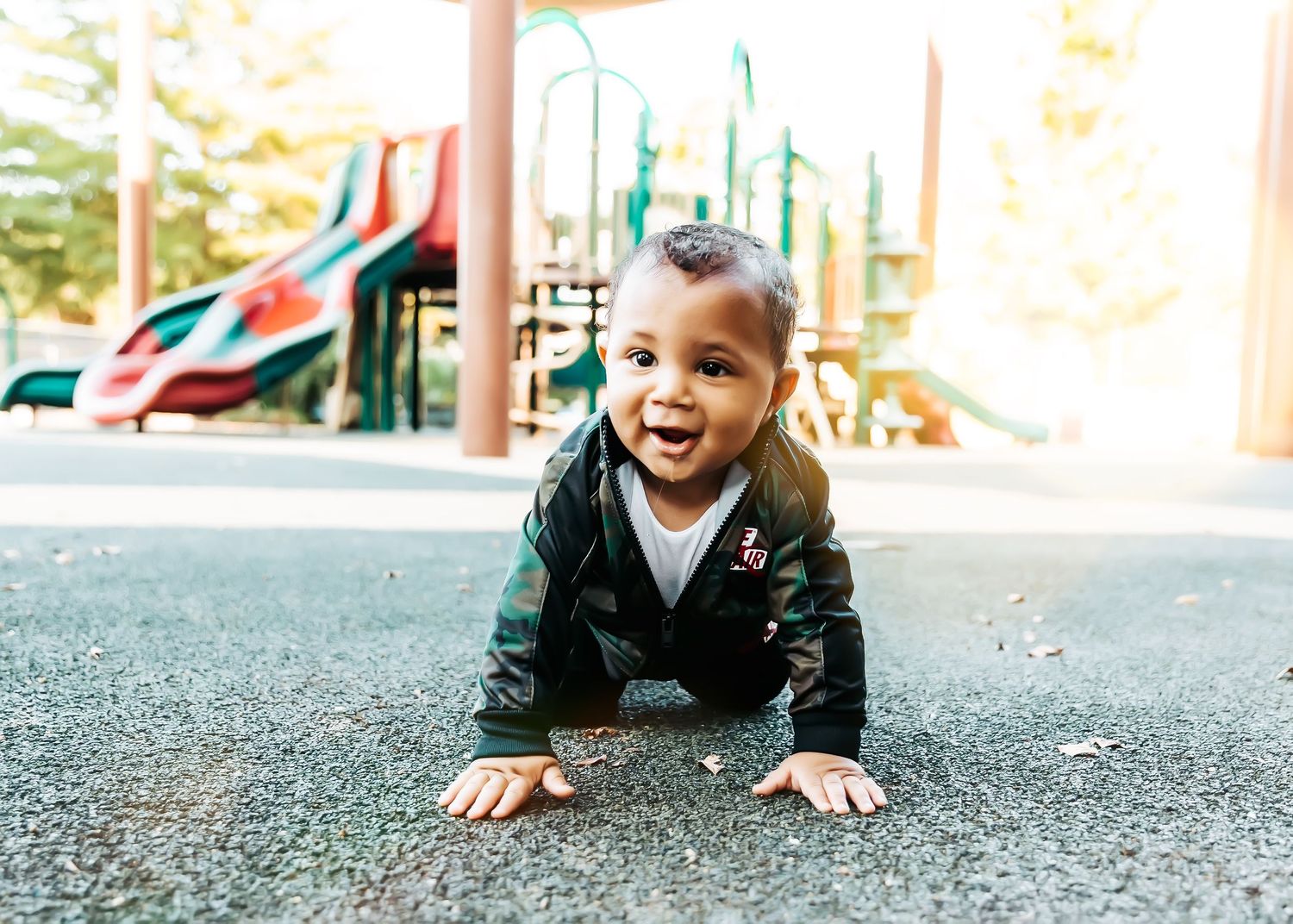 Small child crawls on playground surface wearing navy jacket and white shirt.