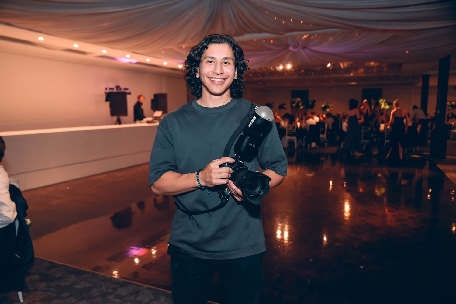 Photographer holding professional camera equipment in dimly lit event venue.