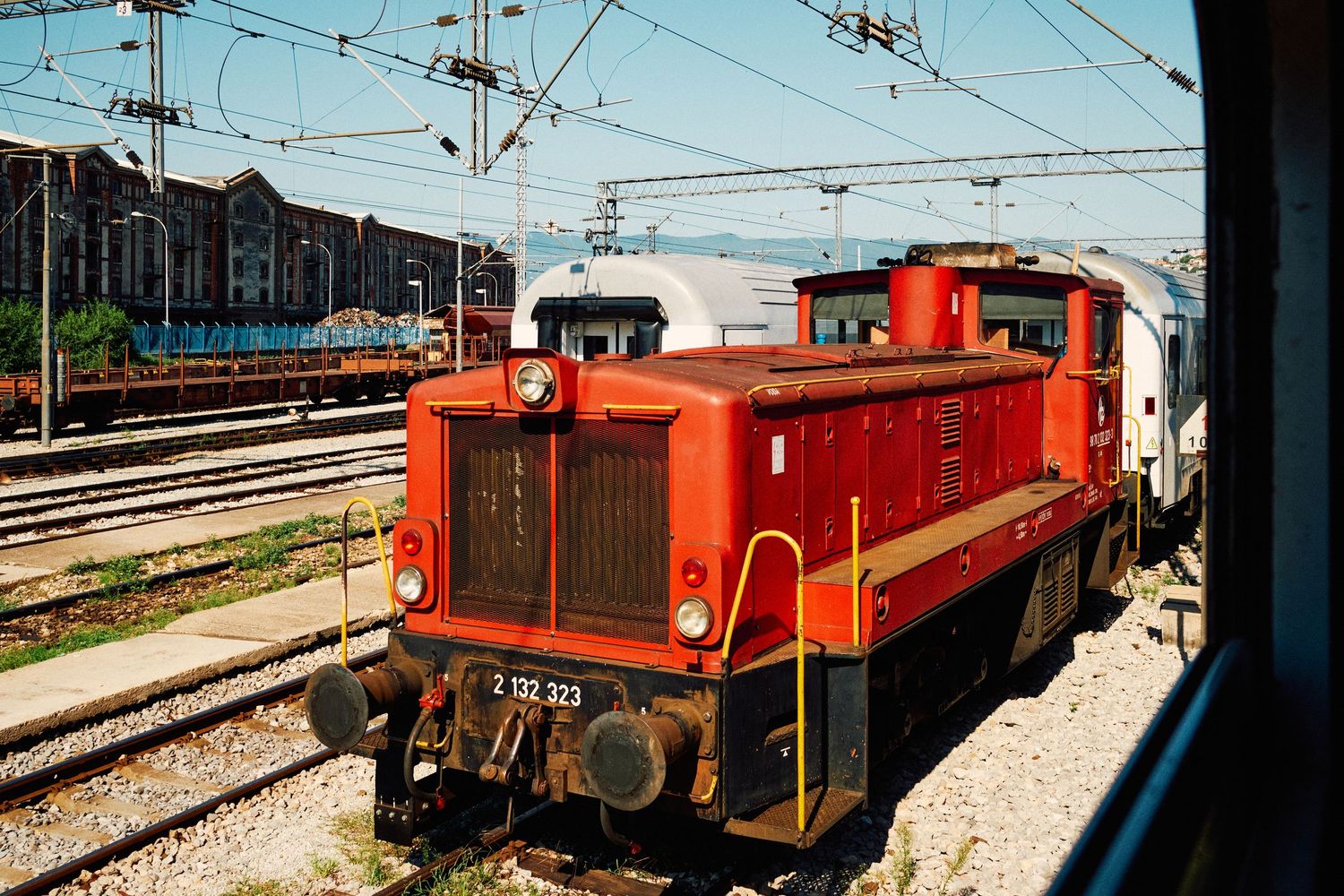 Bright red locomotive engine on railway tracks with industrial buildings in background.