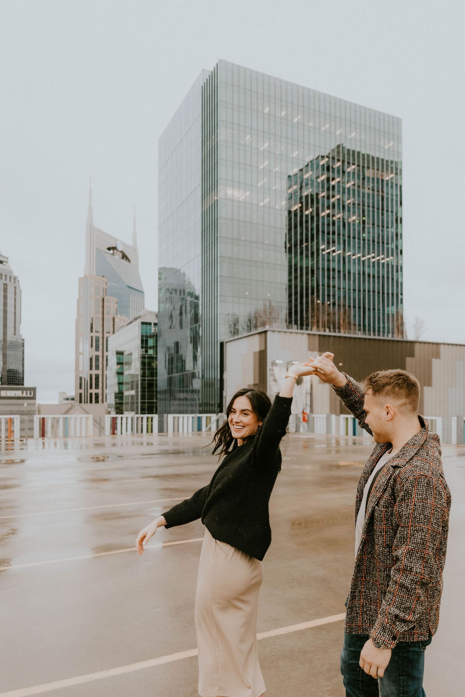 Two people enjoy a playful moment on a rooftop with modern city buildings in the background.
