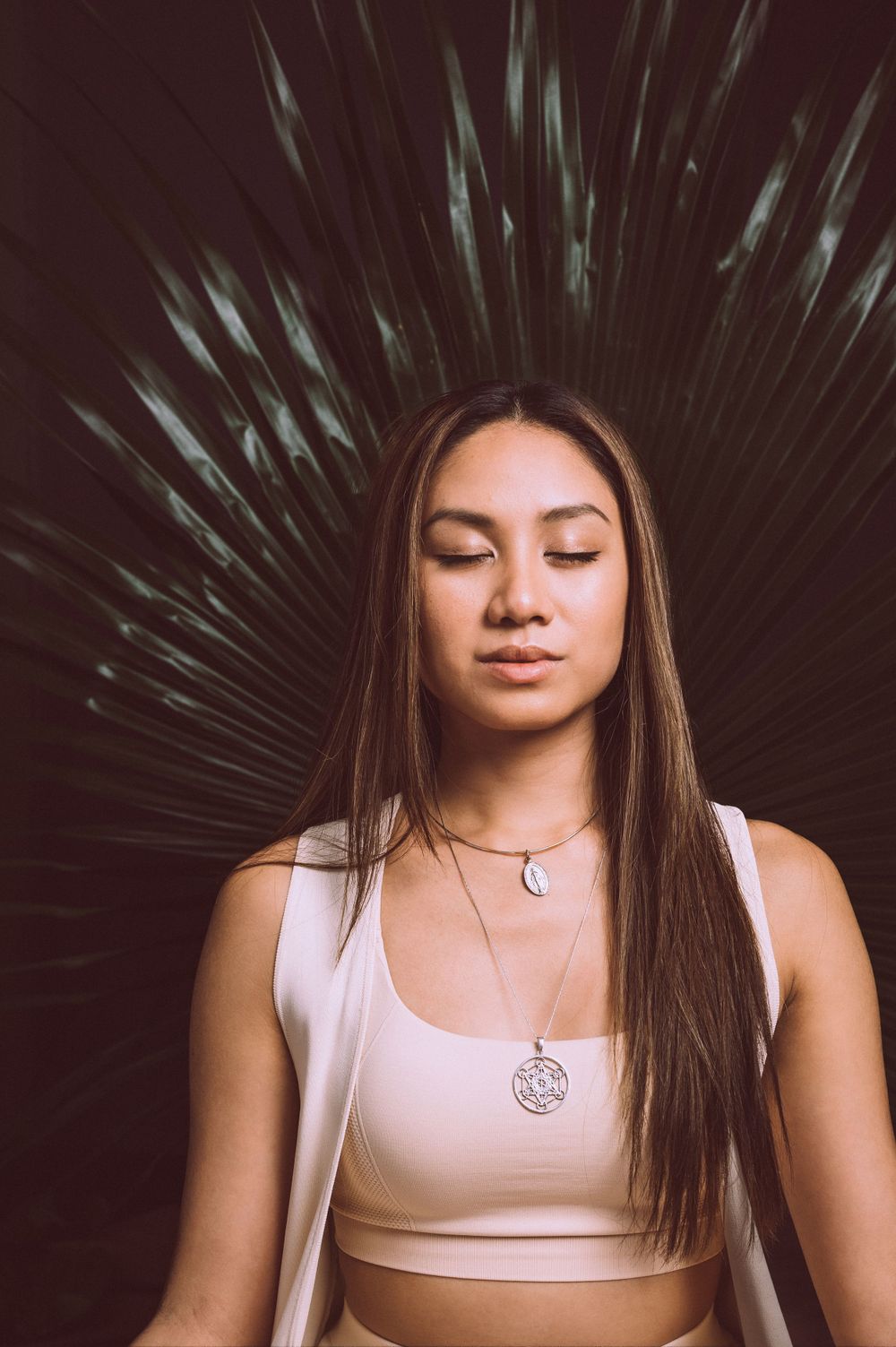 a woman closes her eyes standing in front of a palm leaf