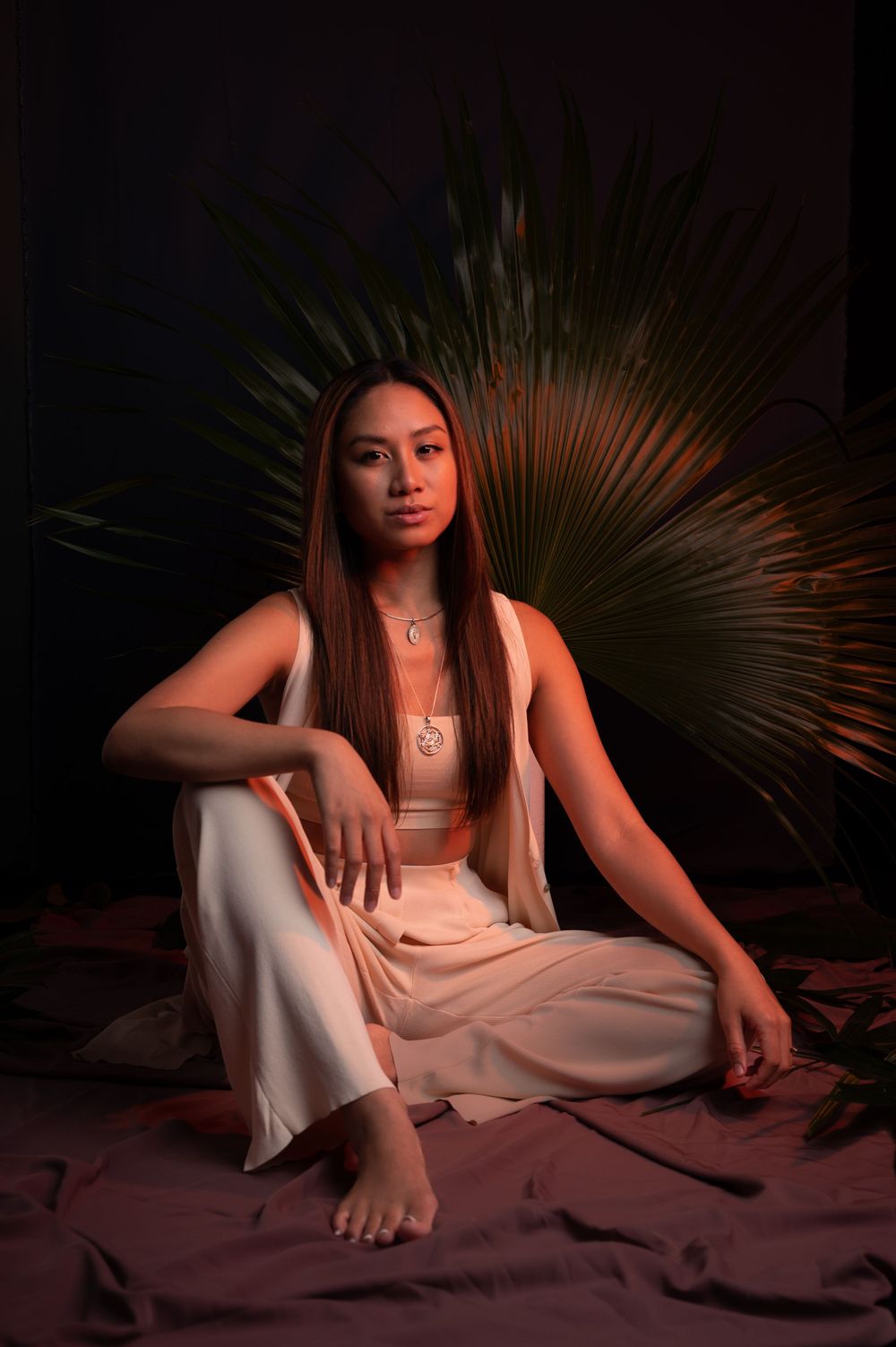 a woman sits in front of a palm frond under orange lights