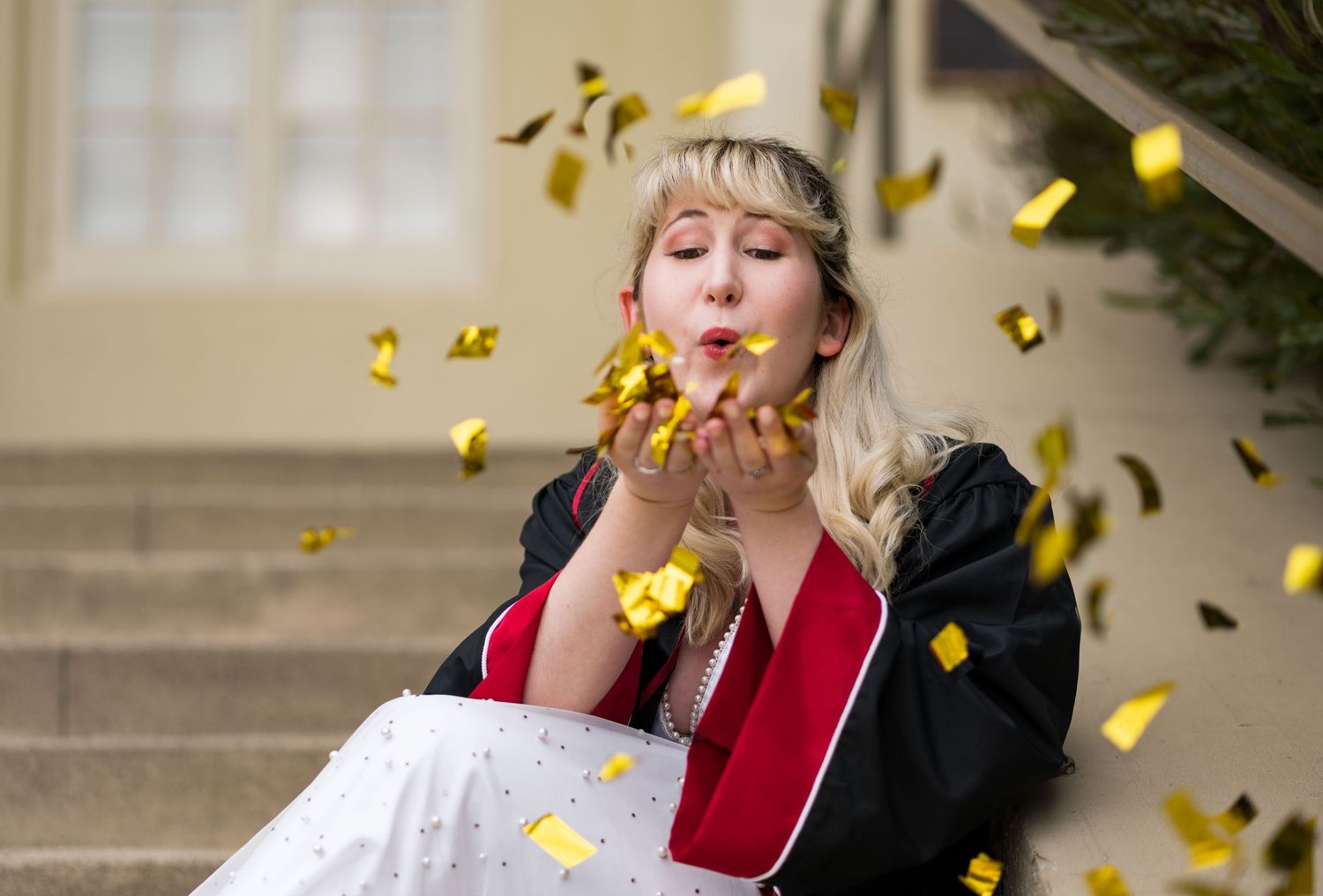 Graduation photo of a Chapman University graduate sitting on steps, blowing gold confetti toward the camera.