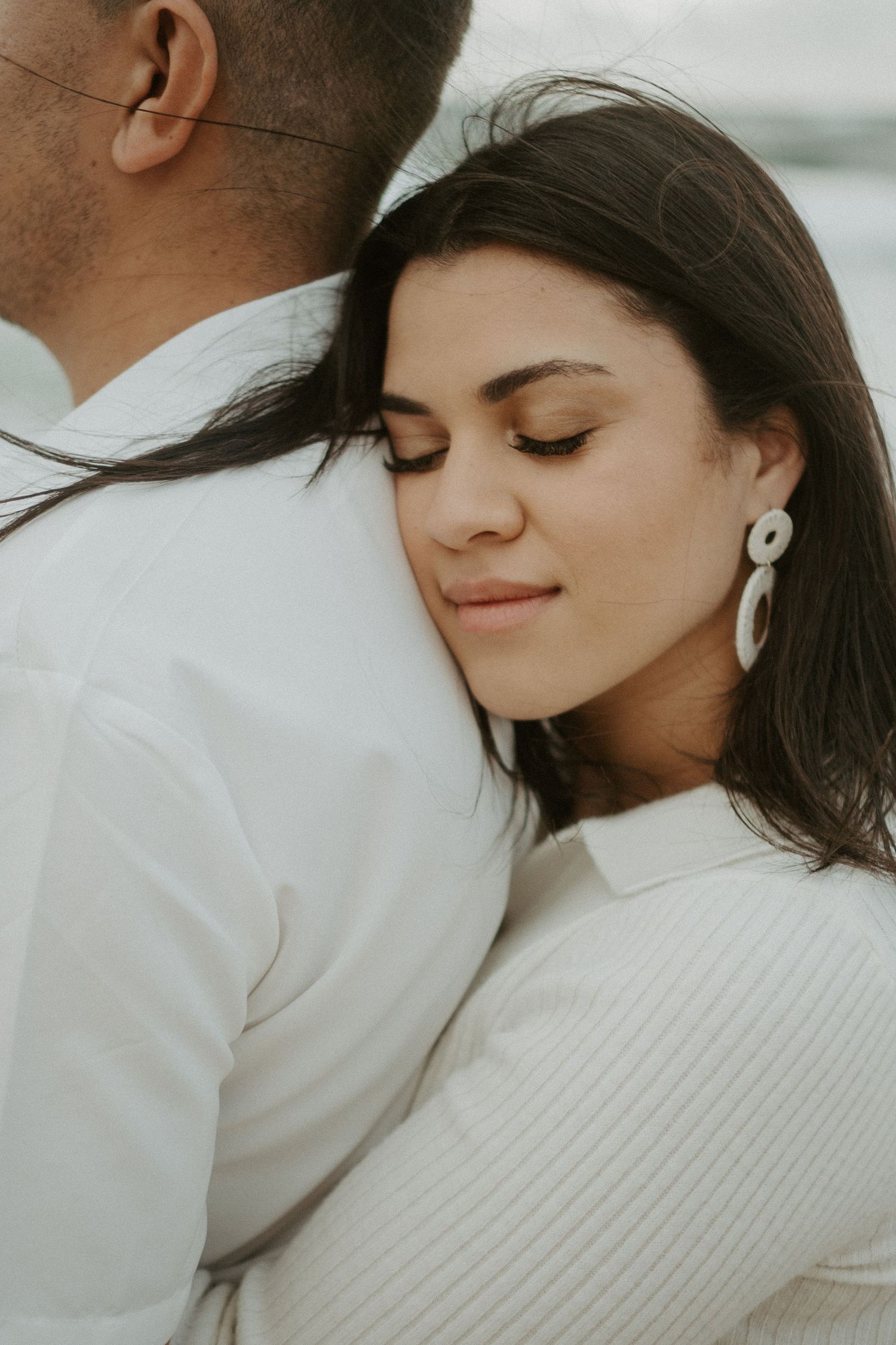 Close up of girl hugging boyfriend from behind with her eyes closed on a windy morning at the beach in Florida