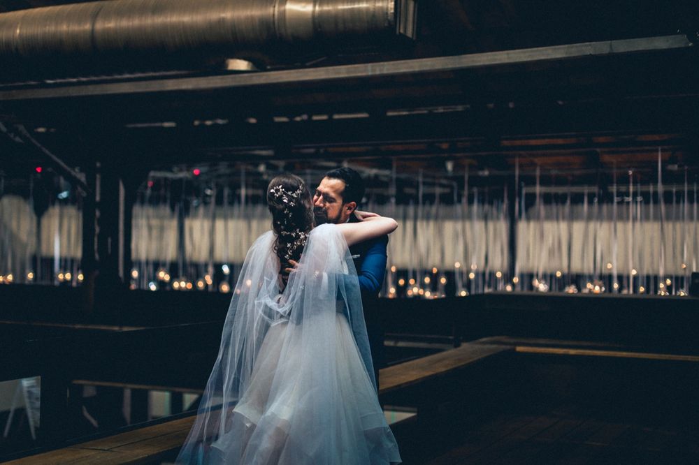 Couple dancing intimately in a dark industrial space with hanging lights in the background.
