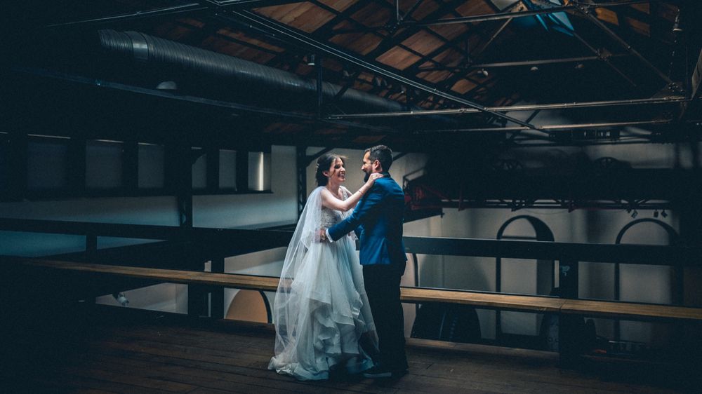 A romantic first dance between newlyweds in an industrial venue with exposed ceiling beams.