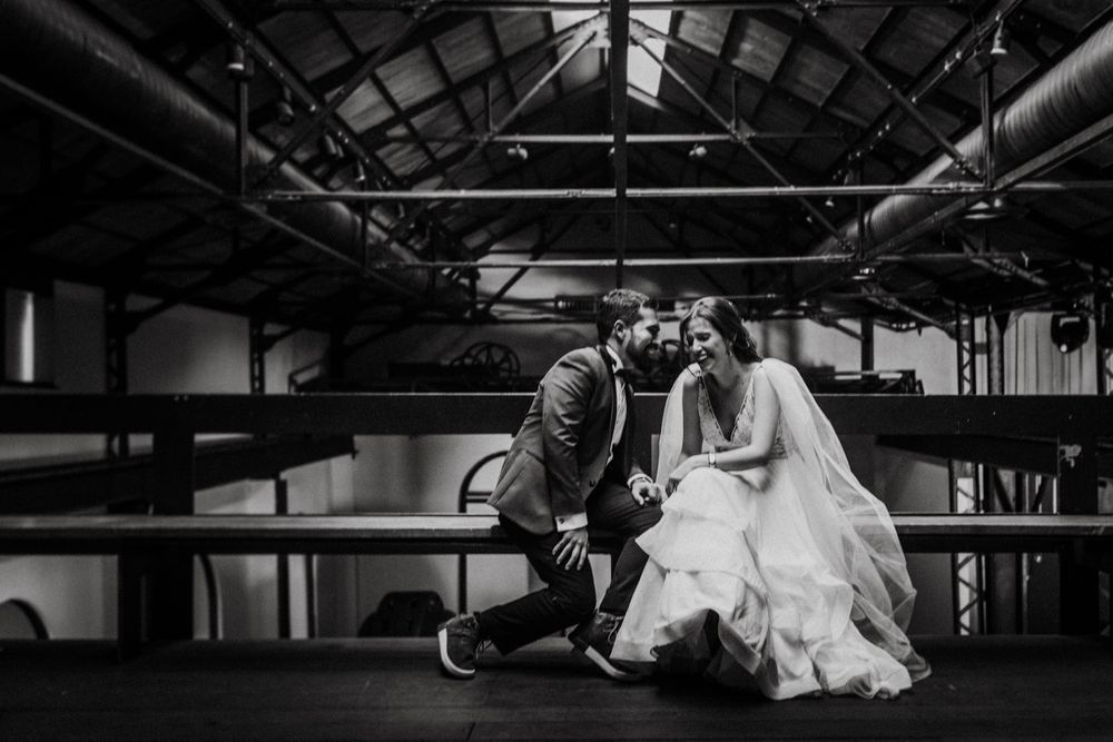 Black and white photo of a wedding couple sharing a playful moment on wooden benches.