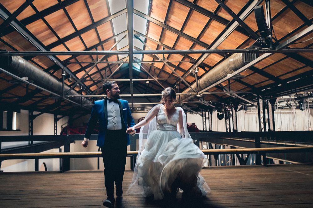 Couple dancing in a rustic venue with wooden beams and high ceilings.