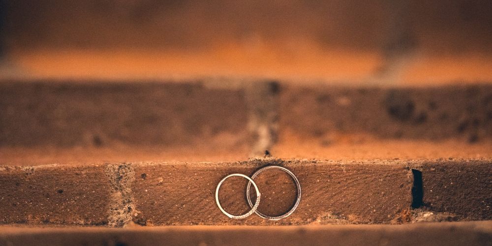 Two wedding rings photographed on a rustic wooden surface against an orange sunset background.