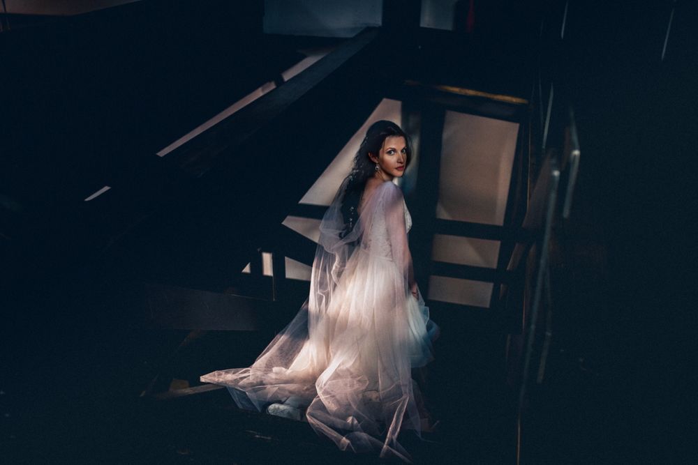 Dramatic bridal portrait on stairs with ethereal lighting and flowing white dress.