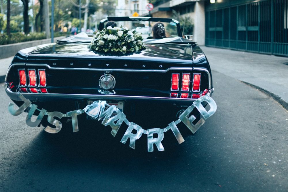 Black vintage Mustang decorated with 'Just Married' sign and floral arrangements.