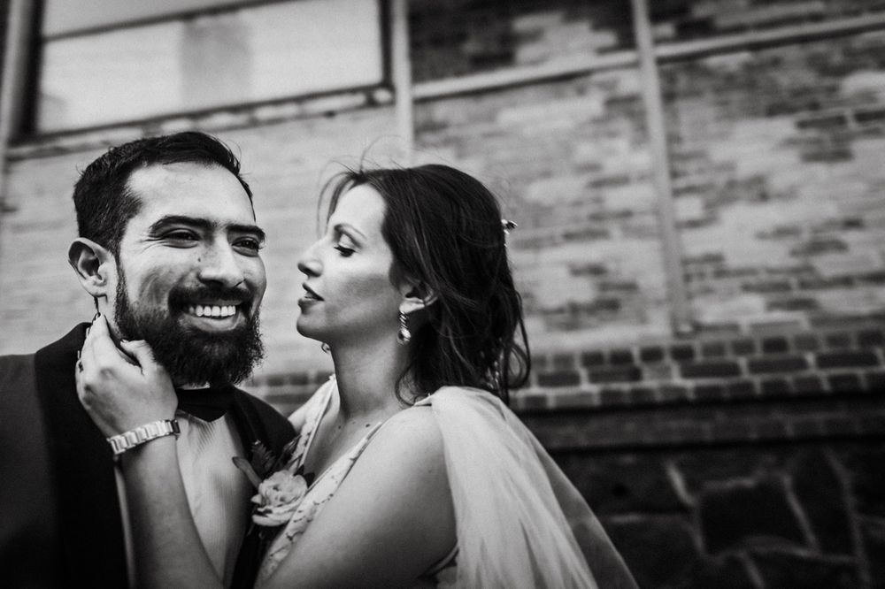 Black and white portrait of joyful couple sharing intimate moment against brick wall.