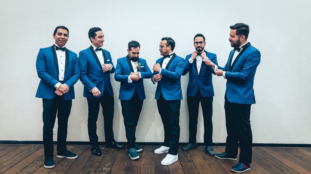 Groomsmen in matching blue suits posing against white wall.