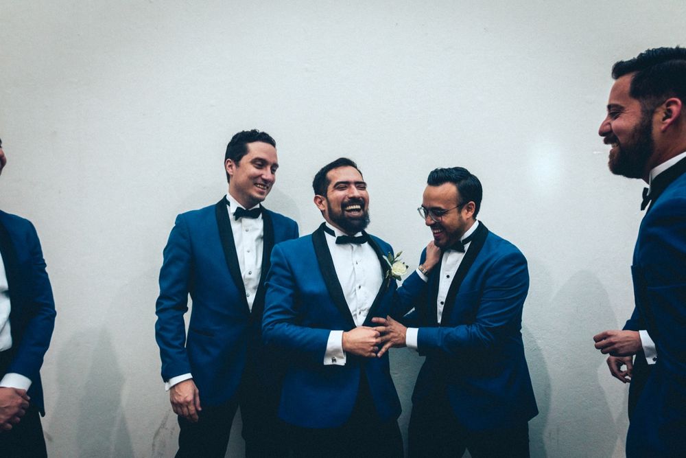 Groomsmen in navy blue suits share laughs and drinks during wedding celebration.