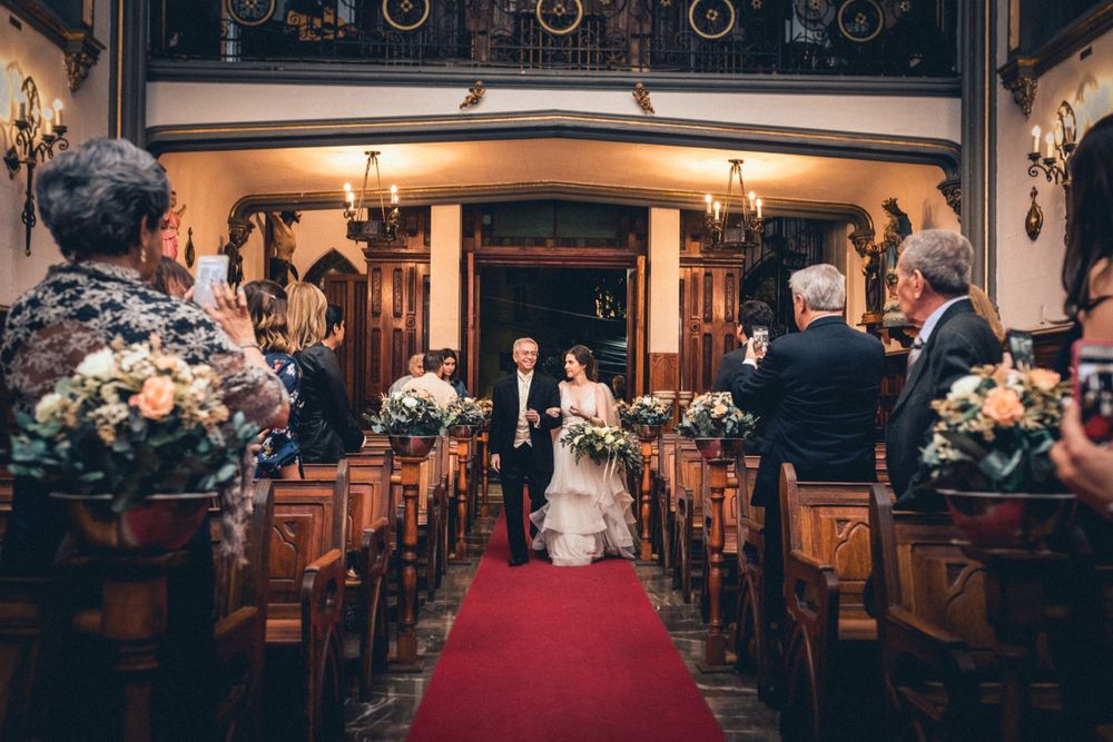 Traditional church wedding ceremony with ornate wooden pews and red carpet aisle.