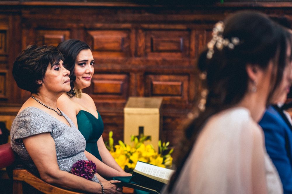 Guests at a formal event seated in wooden pews with yellow floral decorations.