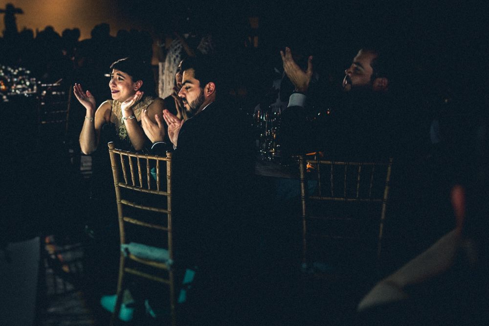 Wedding guests clapping and cheering from their seats during reception celebration.