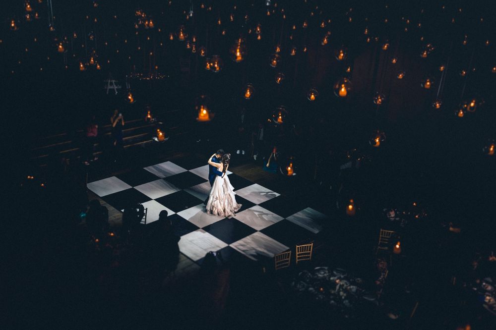 Dramatic overhead shot of couple dancing on illuminated checkered dance floor surrounded by candlelight.