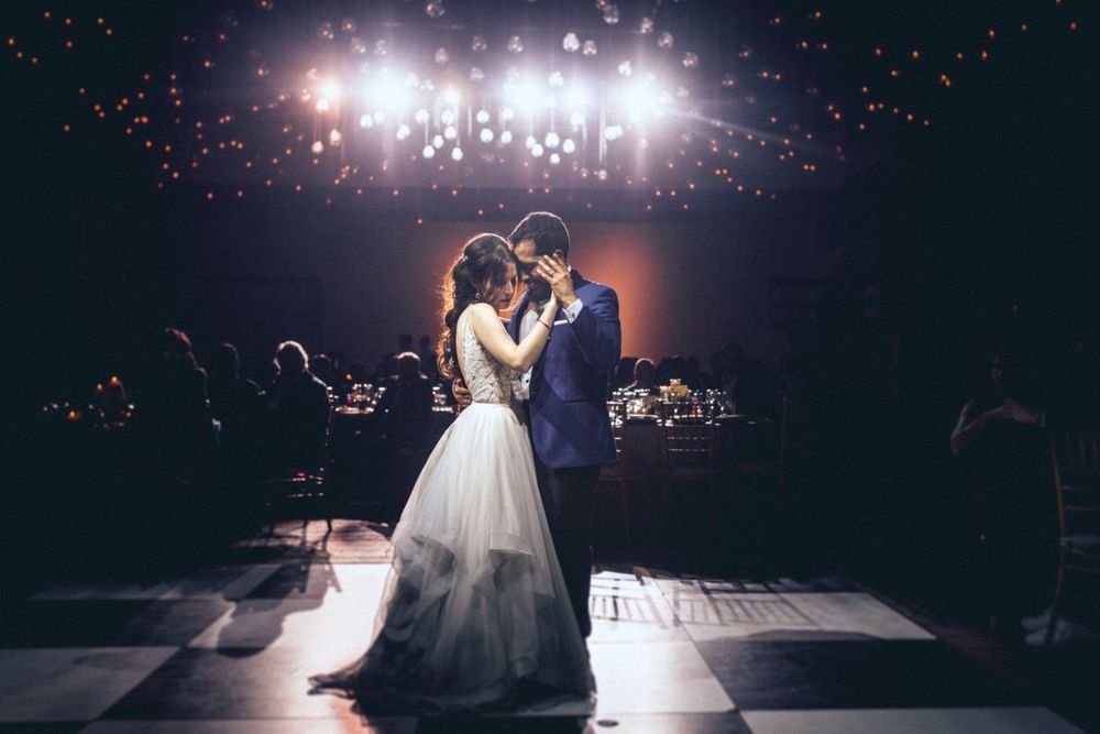 Newlyweds share intimate dance moment under dramatic ceiling lights at wedding reception.