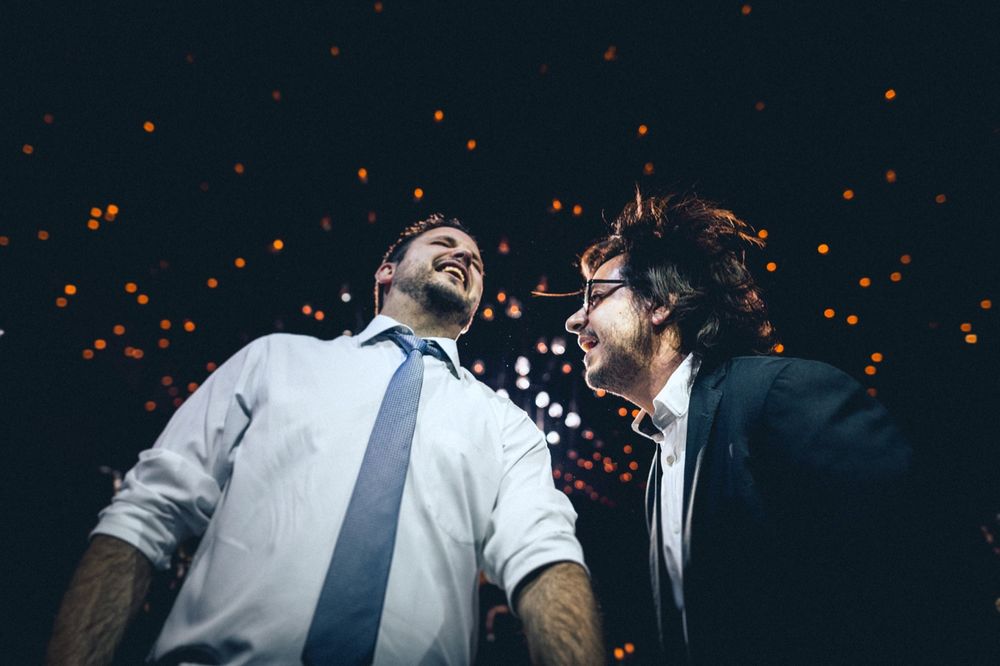 Two guests laughing joyfully with glowing orange lights sparkling in the background at a celebration event.