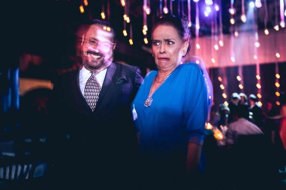 A couple shares a candid moment at a festive party with colorful lights in the background.