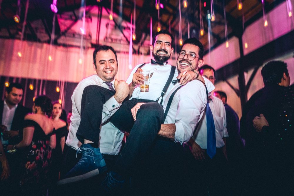 Three party guests pose together under pink lighting at an evening celebration.
