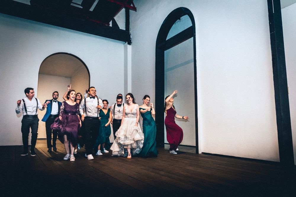 Wedding party members dance in formation on a wooden floor during a celebration.