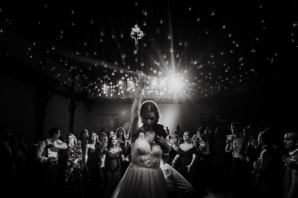 A dramatic black and white shot of a bride dancing under twinkling reception lights.
