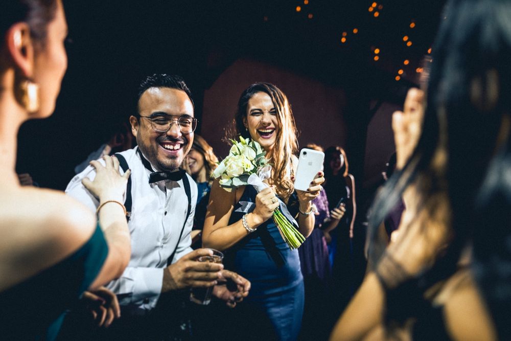 Party guests laugh and celebrate with drinks under ambient lighting at an evening event.
