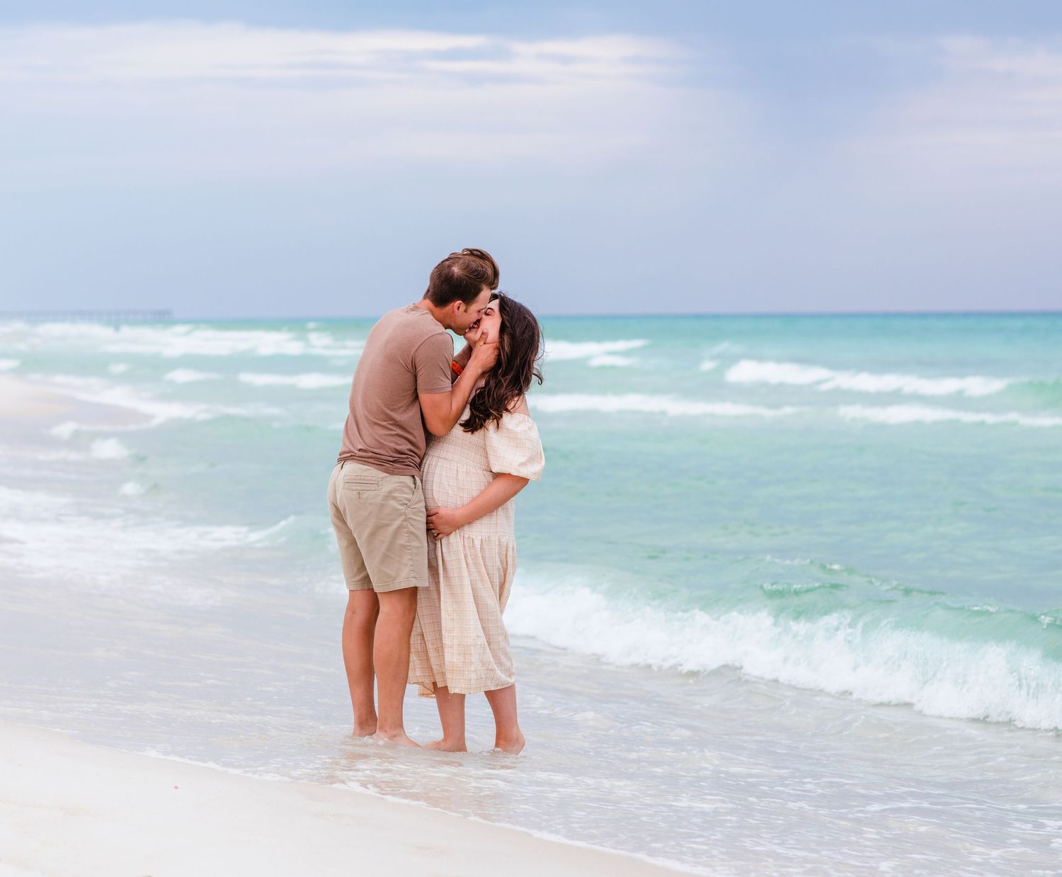 A peaceful embrace between a couple standing at the water's edge on a cloudy beach day.