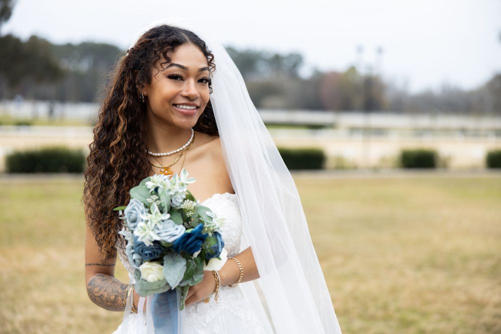 A bride in a white gown holds a blue and white floral bouquet in an outdoor setting.