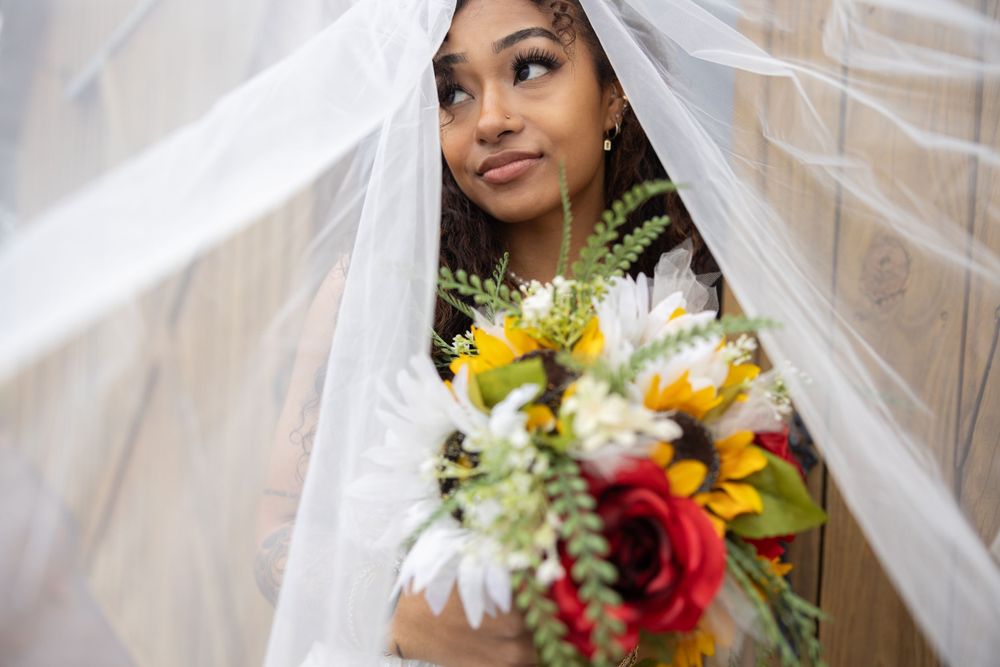 A close-up shot through a veil shows a bride holding a colorful bouquet.